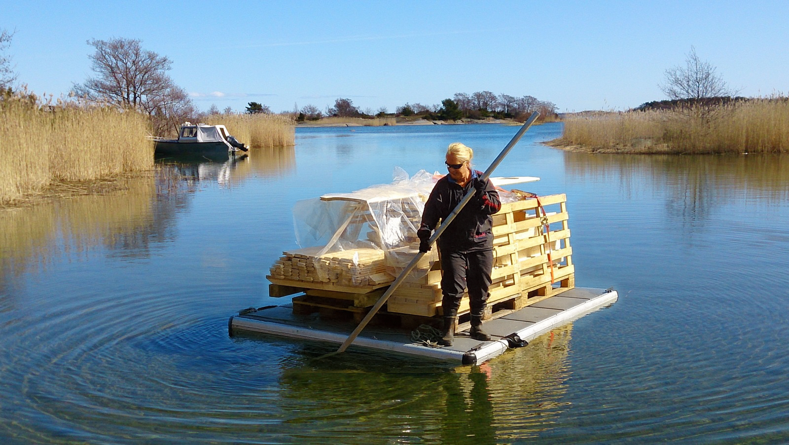 EasyFloat® arbetsflotte med bastu byggd i trädelar på flotten, där en kvinna står vid lasten